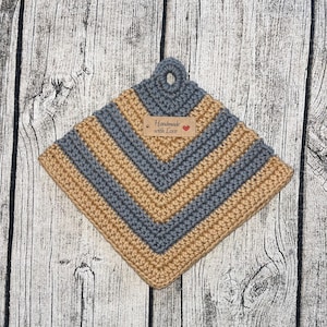 Op de afbeelding: Een grijze en bruine gehaakte ovenwant met een bruin label waarop "Handmade with Love" staat.