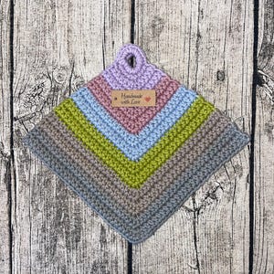 Op de afbeelding: Een handgemaakte, vierkante gehaakte pannenlap met een zigzagpatroon. Het heeft een lus om op te hangen en een label met de tekst "Handmade with Love". Het kleurenschema omvat tinten paars, roze, blauw, groen en grijs.