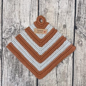Może przedstawiać: Brązowa i biała dziana podkładka pod gorące z wzorem chevron. Podkładka ma pętelkowy uchwyt i brązową metkę z napisem "Handmade with Love" z czerwonym sercem.