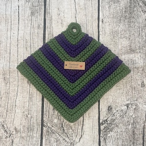 Könnte beinhalten: Ein grüner und lilafarbener gehäkelter Topflappen mit einem braunen Etikett, auf dem "Handmade with Love" steht.