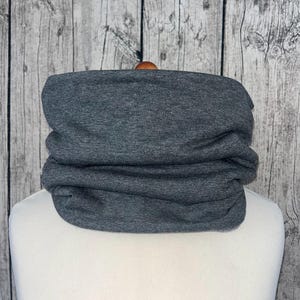 Puede incluir: Un cuello de lana gris o un cuello de lana. El cuello de lana está doblado y se muestra en un maniquí blanco.