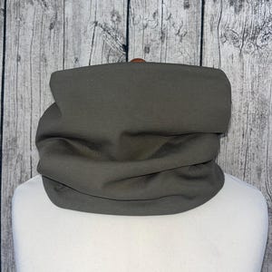 Puede incluir: Un cuello de cuello o bufanda de tela gris oscuro. El cuello de cuello está doblado y se muestra sobre una superficie blanca.