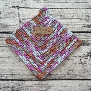 Könnte beinhalten: Ein gehäkelter Topflappen mit einem Chevron-Muster in Pink, Weiß und Braun. Er hat einen Schlaufe-Griff und ein braunes Etikett mit der Aufschrift "Handmade with Love".