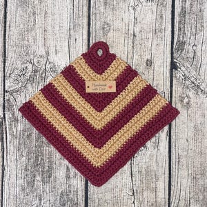 Könnte beinhalten: Ein gehäkelter Topflappen in Burgunderrot und Beige mit einem braunen Etikett mit der Aufschrift "Handmade with Love".