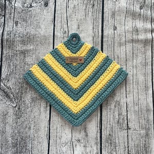 Peut inclure: Un dessous de plat fait à la main en crochet, de forme carrée. Le dessous de plat présente un motif en chevrons en bleu sarcelle et jaune. Une petite étiquette avec les mots "Handmade with Love" est attachée. Le dessous de plat a une boucle pour l'accrocher.