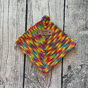 Könnte beinhalten: Ein bunter gehäkelter Topflappen mit einem braunen Etikett, auf dem "Handmade with Love" und ein rotes Herz stehen.