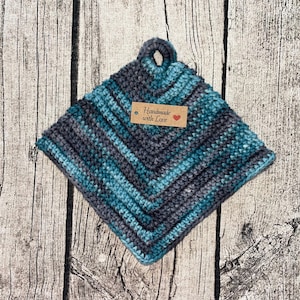 Op de afbeelding: Een blauwe en grijze gehaakte ovenwant met een bruin label waarop "Handmade with Love" staat.