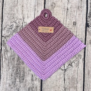 Könnte beinhalten: Ein lila und pinkfarbener gehäkelter Topflappen mit einem braunen Etikett, auf dem "Handmade with Love" und ein rotes Herz steht.