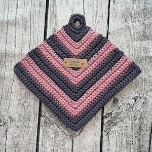 Könnte beinhalten: Ein gehäkelter Topflappen mit einem gestreiften Muster in Rosa und Grau. Er hat eine Schlaufe oben zum Aufhängen. Der Topflappen hat ein Etikett mit der Aufschrift "Handgefertigt mit Liebe".