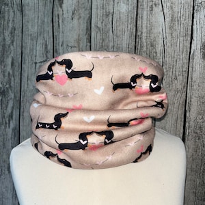 Könnte beinhalten: Ein beiger Nackenschutz mit einem sich wiederholenden Muster aus schwarzen Dackeln, die sich küssen, und rosa Herzen.