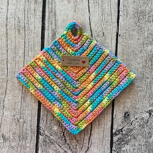 Peut inclure: Un dessous-de-plat carré fait à la main au crochet, aux couleurs vives : bleu, vert, orange, rose et jaune. Le dessous-de-plat présente un motif en chevrons et une petite étiquette avec l'inscription "Handmade with Love".