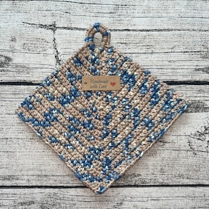 Könnte beinhalten: Ein gehäkelter Topflappen in Beige und Blau mit einem braunen Etikett, auf dem "Handmade with Love" und ein rotes Herz stehen.