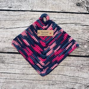 Peut inclure: Un dessous de plat crocheté dans des tons de rose, bleu et violet avec une étiquette brune qui indique "Fait main avec amour".