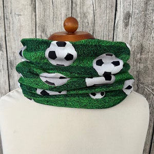 Könnte beinhalten: Ein grüner Nackentuch mit einem Fußballmuster. Der Nackentuch ist aus einem weichen, dehnbaren Stoff gefertigt und perfekt, um im Winter warm oder im Sommer kühl zu bleiben.