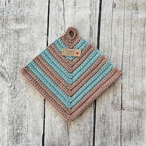 Peut inclure: Un dessous de plat crocheté en brun et bleu sarcelle avec une étiquette brune indiquant "Handmade with Love" et un cœur rouge.