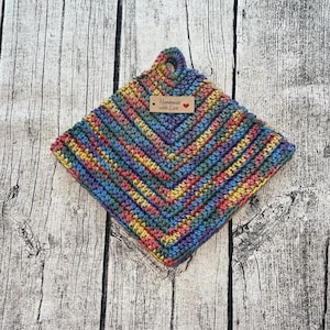 Op de afbeelding: Een handgemaakte, vierkante gehaakte pannenlap met een chevronpatroon. De pannenlap heeft een lus om op te hangen en een klein label met de tekst "Handmade with Love". Het kleurenpalet omvat tinten blauw, geel, roze en paars.