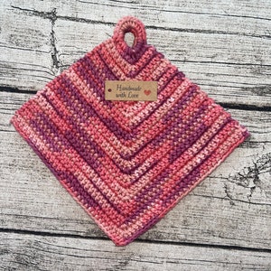 Könnte beinhalten: Rosa und lila gehäkelter Topflappen mit einer Aufhängeschlaufe und einem braunen Etikett mit der Aufschrift "Handmade with Love".