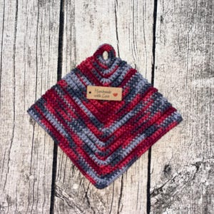 Może przedstawiać: Czerwono-szary uchwyt na garnek wykonany na szydełku z pętlą. Uchwyt na garnek ma małą brązową metkę z napisem "Handmade with Love" i czerwonym sercem.