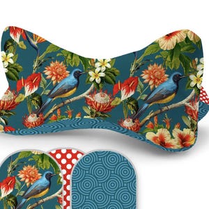 Può includere: Un cuscino decorativo con uno sfondo verde acqua che presenta un vivace motivo floreale e di uccelli. Il design include uccelli blu, fiori arancioni e fogliame verde. Campioni di tessuto abbinati aggiuntivi sono visibili sotto.