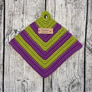 Op de afbeelding: Een groene en paarse gehaakte ovenwant met een bruin label waarop "Handmade with Love" en een rood hartje staat.