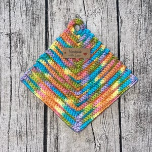 Op de afbeelding: Een kleurrijke gehaakte ovenwant met een bruin label waarop "Handmade with Love" staat.