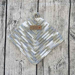 Könnte beinhalten: Ein gehäkelter Topflappen in einem Rautenmuster mit grauem, weißem und beigefarbenem Garn. Der Topflappen hat eine Schlaufe oben und ein braunes Etikett mit der Aufschrift "Handmade with Love".