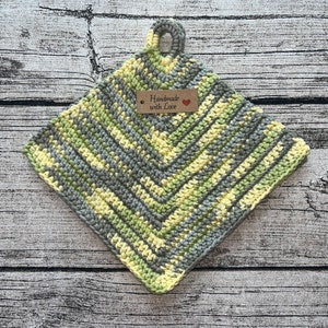 Könnte beinhalten: Ein grauer und gelber gehäkelter Topflappen mit einer Schlaufe. Der Topflappen hat ein braunes Etikett mit der Aufschrift "Handmade with Love" und einem roten Herzen.