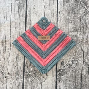 May include: A handmade, square crochet potholder in shades of grey and coral pink. The design features chevron stripes and a loop for hanging. A small tag reads "Handmade with Love".
