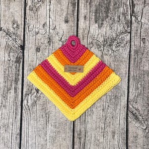 Könnte beinhalten: Ein gehäkelter Topflappen in Gelb, Orange und Pink mit einem braunen Etikett, auf dem "Handmade with Love" steht.