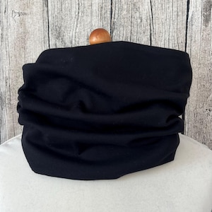 Peut inclure: Un tour de cou en tissu noir, doux et extensible. Le tour de cou est plié et présenté sur un mannequin blanc.