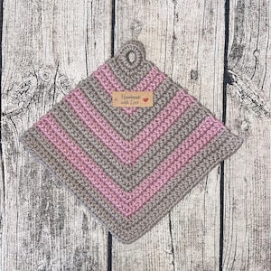 Op de afbeelding: Een gehaakte ovenwant met een gestreept patroon in roze en bruin. Het heeft een lus aan de bovenkant en een bruin label met de tekst "Handmade with Love".