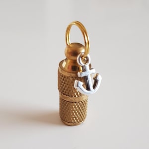 Könnte beinhalten: Ein goldfarbener Hundemarkenanhänger aus Metall mit einem kleinen silbernen Anker-Anhänger. Die Marke hat ein Gewinde oben und einen Ring zum Befestigen an einem Halsband.