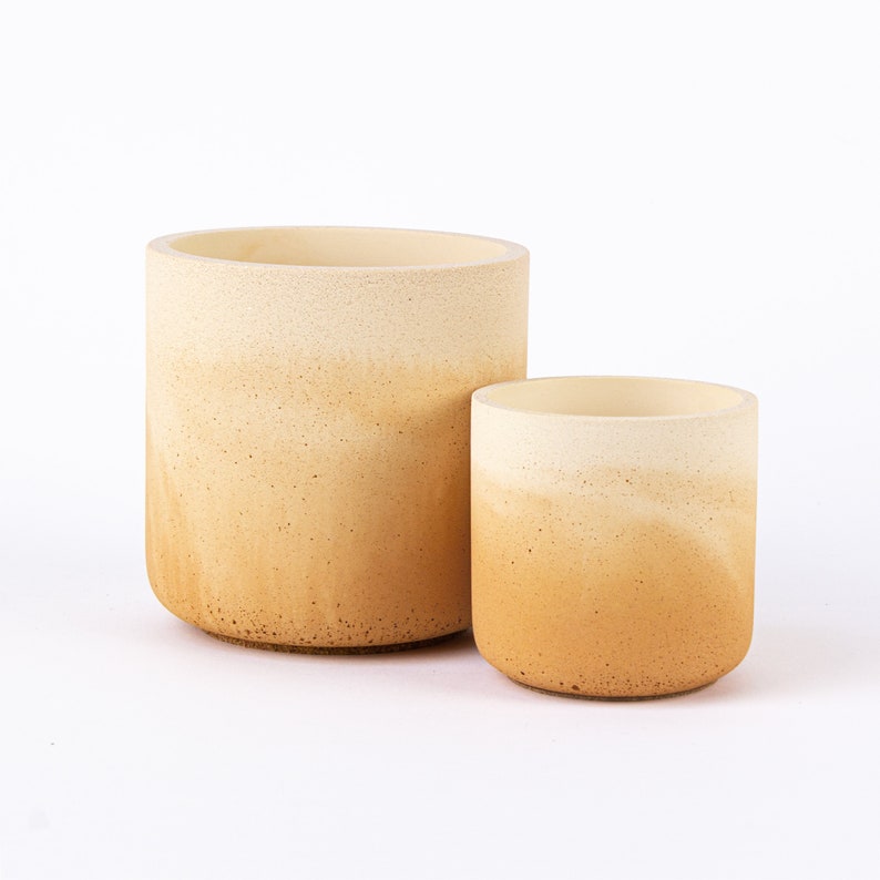 May include: Two ombre ceramic planters, one larger than the other, with a light beige to brown gradient. The planters are made of a textured material and have a rounded shape.