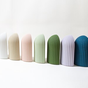 May include: A set of ten ceramic arched-shaped decorative objects in various colors, including white, beige, pink, green, light purple, and blue.