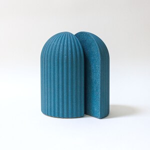 May include: A pair of blue ceramic bookends shaped like arches. The bookends have a textured surface and are a modern design.