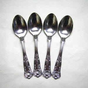 May include: Four silver spoons with oval bowls and decorative, floral-patterned handles. The spoons are arranged in a row, reflecting light. The handles have a detailed design, adding a touch of elegance to the silverware.