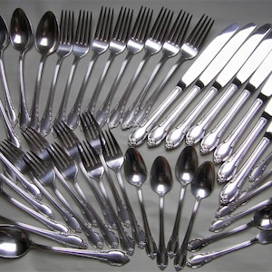 May include: A set of cutlery, including forks, spoons, and knives, arranged in a fan shape. The cutlery is made of polished silver and has a decorative design.