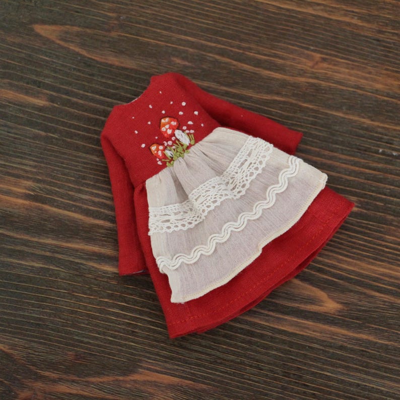 May include: A red linen doll dress with embroidered mushrooms and a white lace trim.