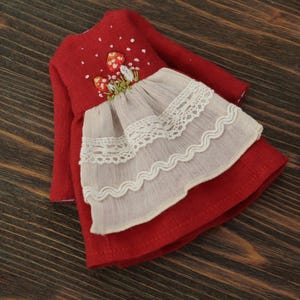 May include: A red linen dress with embroidered mushrooms and white lace trim. The dress has long sleeves and a gathered skirt.
