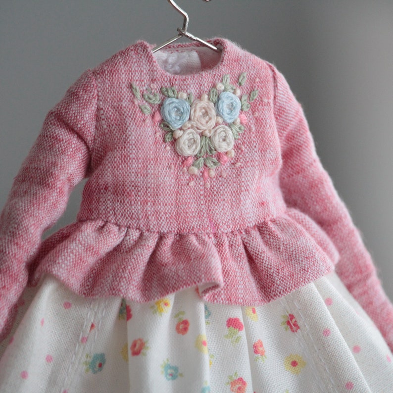 May include: A pink knitted dress with a ruffled skirt and a floral embroidered bodice. The dress has a white and floral print skirt.