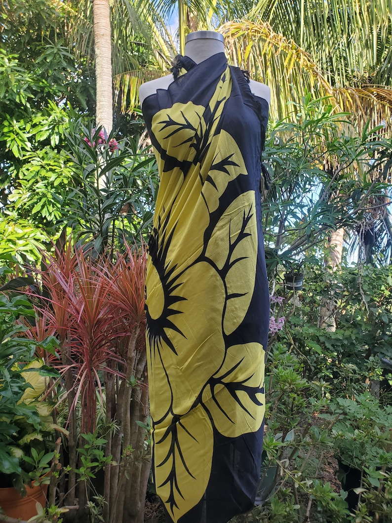 Puede incluir: Sarong negro con un gran estampado de flor de hibisco amarilla. El sarong est&aacute; drapeado sobre un maniqu&iacute;.