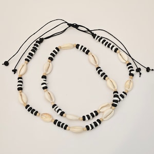 May include: A black and white shell necklace with a black cord. The necklace is made of small, oval-shaped shells and black beads.