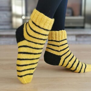 May include: A pair of yellow and black striped socks with black heels and toes. The socks are knitted and have a casual look.