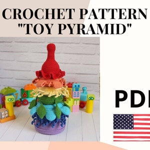 Puede incluir: Patrón de crochet para una pirámide de juguete colorida, con un esquema de colores rojo, naranja, amarillo, verde, azul y morado. El patrón está disponible para descargar en PDF. La imagen también incluye una pequeña bandera estadounidense.