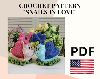 May include: Crochet pattern for two snails in love, one pink and one blue, with hearts on their shells. The pattern is available as a PDF download. The image also includes the text "CROCHET PATTERN "SNAILS IN LOVE" PDF"