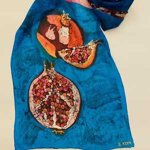 Può includere: Sciarpa di seta con un vivace design a melograno. La sciarpa presenta uno sfondo blu con melograni arancioni e rossi. La sciarpa è firmata "S. KERN" nell'angolo in basso a destra. La sciarpa è piegata e drappeggiata.