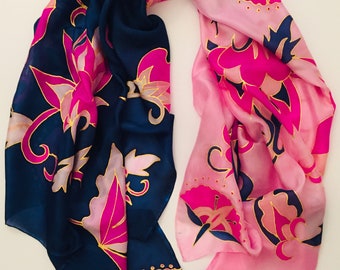 May include: A silk scarf with a floral design. The scarf is divided into two sections, one navy blue and the other light pink. The floral pattern features pink and gold accents. The scarf is a fashion accessory.