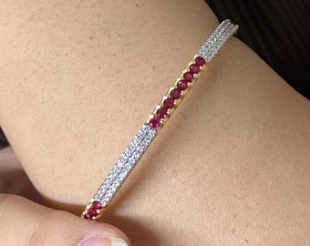 May include: A gold bangle bracelet with a row of red gemstones and a row of clear gemstones.