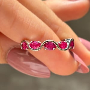 May include: A silver ring featuring a series of oval-cut, vibrant red gemstones. The gemstones are set in a wavy, continuous design, creating a flowing and elegant look. The ring is a piece of jewelry.