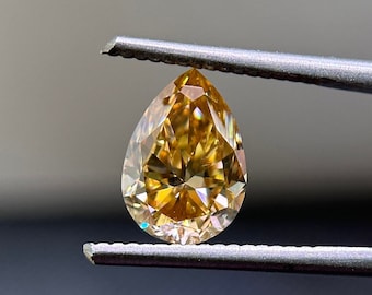 May include: A pear-shaped, yellow diamond gemstone held by tweezers. The diamond has a brilliant cut and facets that reflect light.